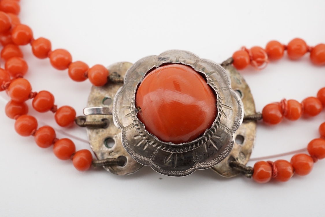 A triple strand graduated coral bead choker necklace, with a cabochon coral set white metal clasp, 38cm.